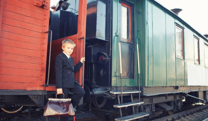 little boy with a suitcase standing in the retro train